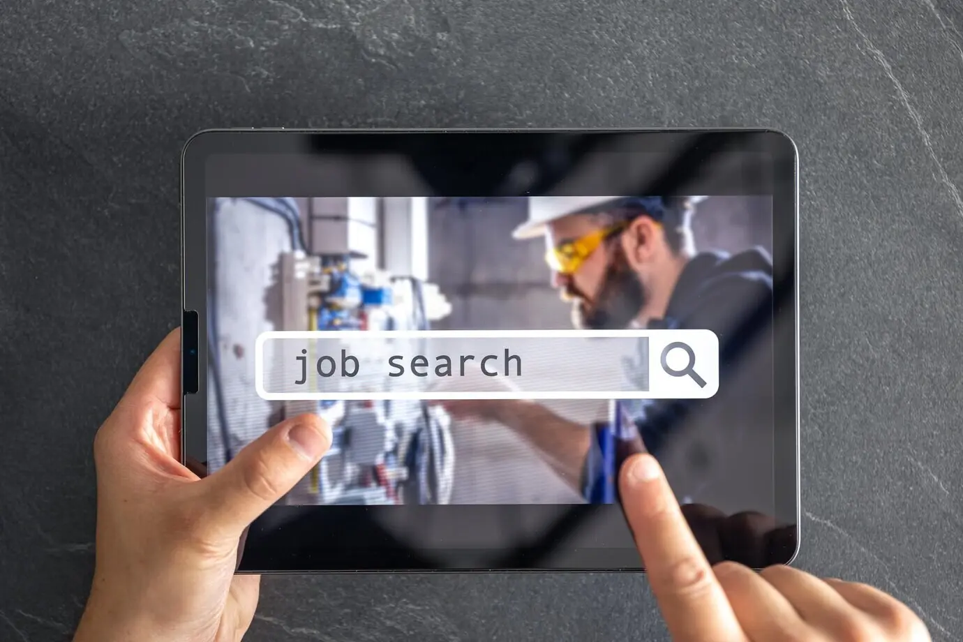 Top-down view of a digital tablet with a job search on its screen, held in male hands.