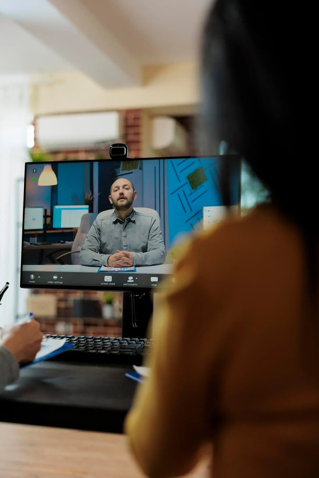 Female entrepreneur reading a recruiter’s CV and discussing a hiring application with a remote potential worker during an online video call conference in a startup office. Teleconference call visible on the computer screen.