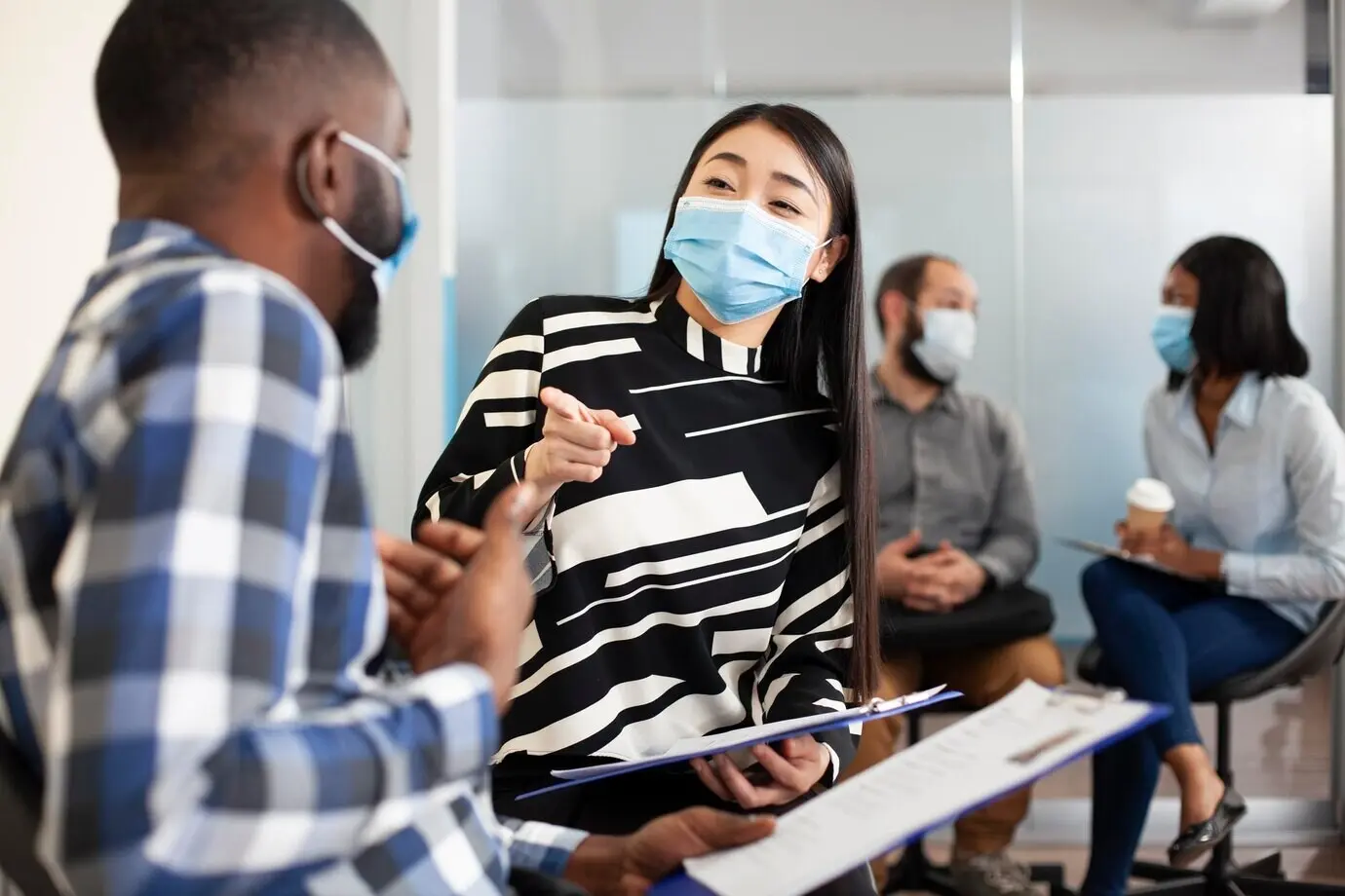 A masked man and a woman converse in a lobby.